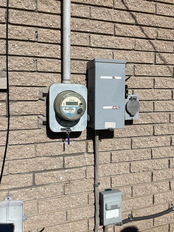 Conducted on-site electrical assessment for whole-house generator installation. Evaluated existing electrical infrastructure including main service panel containing approximately 20-24 circuit breaker positions and exterior meter base with digital meter and associated disconnect equipment. Documented current electrical configuration, photographed panel interior showing dual columns of circuit breakers and circuit directory, and assessed exterior service entrance components mounted on brick wall including meter enclosure, junction boxes, and conduit routing to determine load capacity and integration requirements for proposed generator system.