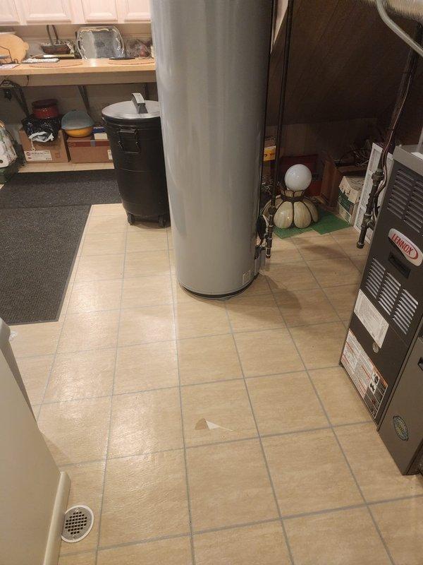 Documented tile floor damage in utility room where HVAC equipment is installed. Captured multiple photographs from various distances and angles showing affected beige tile flooring around water heater and HVAC unit, including close-up and wide-angle views to document extent of damage for records.