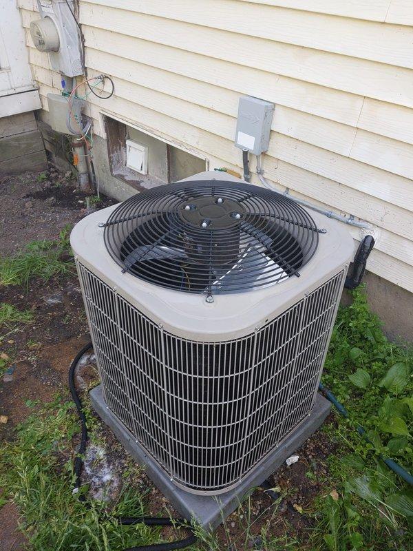 Completed scheduled AC maintenance on residential outdoor condensing unit. Performed comprehensive system inspection including visual examination of condenser coils, fan assembly, and electrical components. Unit found in operational condition with cylindrical condenser positioned on pad against exterior wall. Verified proper fan operation, checked refrigerant line connections, and inspected electrical disconnect box. Documented equipment condition with photographs showing unit placement, surrounding area, and overall system configuration. All maintenance tasks completed per manufacturer specifications and industry standards.