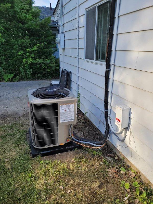 Completed installation of Bryant air conditioning system with downflow configuration at residential property. Installed new condensing unit on exterior platform pad with proper leveling and positioning. Replaced existing lineset with new refrigerant lines, routing copper piping and insulation along exterior wall with secure mounting brackets. Connected gray insulated refrigerant lines from condenser to interior air handler. Installed gray electrical disconnect box on exterior wall per code requirements. Mounted and programmed Ecobee6 smart thermostat to control new system. Ran condensate drain line using white PVC piping from air handler to exterior discharge point. Verified all electrical connections, tested system operation through complete cooling cycle, and confirmed proper refrigerant charge and airflow. System commissioned and left in fully operational condition.