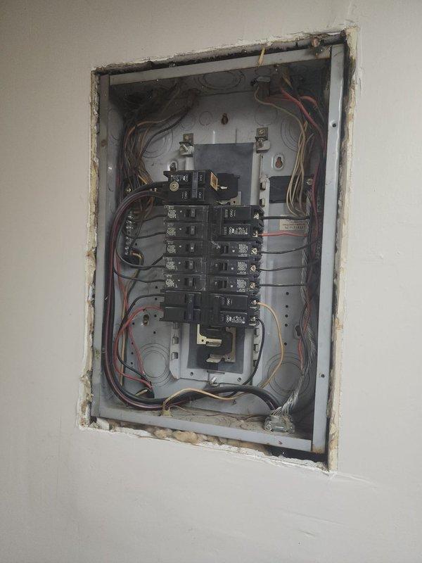 Returned to site to assess remaining work required for AC10 electrical box installation. Inspected electrical panel configuration with exposed breakers and wiring connections, and evaluated outdoor condenser unit with refrigerant lines and attached diagnostic gauges to determine completion status of system integration.