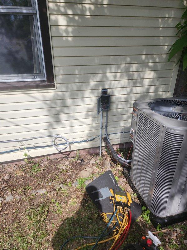 Returned to site to assess remaining work required for AC10 electrical box installation. Inspected electrical panel configuration with exposed breakers and wiring connections, and evaluated outdoor condenser unit with refrigerant lines and attached diagnostic gauges to determine completion status of system integration.