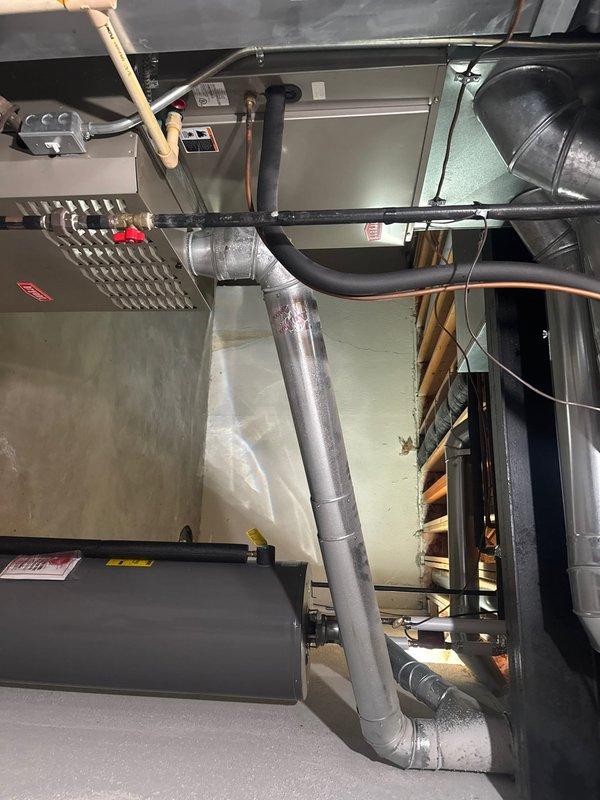 Responded to service call for leaking humidifier on HVAC system. Upon arrival, inspected Aprilaire whole-home humidifier mounted to supply ductwork. Identified active water leak from humidifier unit, which was determined to be approximately 5-10 years old. Examined humidifier water feed line, solenoid valve, drain connection, and evaporator pad assembly for source of leak. Checked water panel frame and housing for cracks or deterioration. Verified furnace and air conditioning system operation—both heating and cooling functions performing normally with no other deficiencies noted. Documented existing installation with photographs showing humidifier mounted to metallic supply plenum with proper ducting connections. Provided customer with findings and repair recommendations to address the water leak issue.