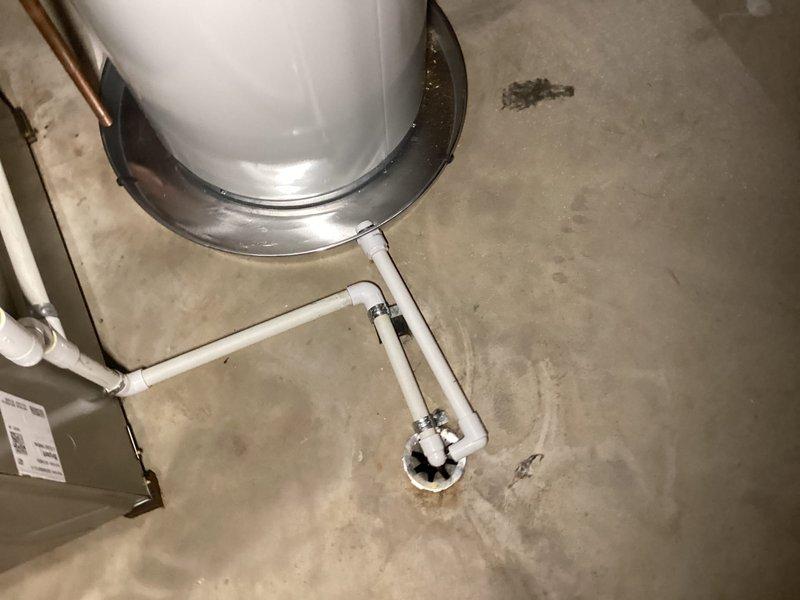 Completed installation of a 40-gallon Bradford White residential water heater in utility area. Installation included proper venting with metallic flex duct, connection of copper supply lines with brass fittings and shut-off valves, installation of blue expansion tank, yellow-handled gas valve, pressure relief valve, and PVC drain pan piping system connected to floor drain.