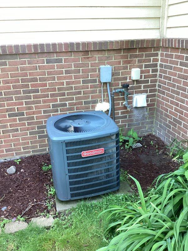 Assessed non-functional 6-year-old Goodman air conditioning unit with failed compressor located on exterior concrete pad against brick wall. Evaluated existing electrical service at breaker panel and documented current system configuration including refrigerant lines and drainage piping. Provided comprehensive replacement estimate for new AC system to restore residential cooling capacity.