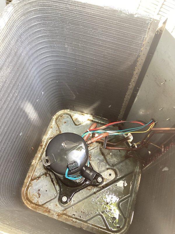 Responded to no cooling complaint on aging residential air conditioning system. Upon inspection, found unit blowing warm air with compressor not operating. Diagnosed failed compressor motor with visible corrosion on base pan and electrical connections. Unit showed significant age-related wear including deteriorated drain pan and accumulated debris. Advised customer of compressor failure and provided replacement options for the 10+ year old system.