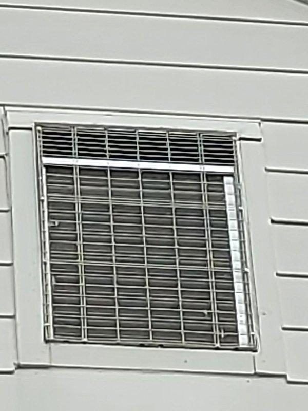 Responded to no cooling call for window-mounted air conditioning unit. Upon arrival, found unit appeared to be running but producing no airflow to interior space. Inspected exterior-mounted window AC unit with white frame and protective metal louver grille. Diagnosed complete airflow blockage preventing conditioned air from reaching living space. Cleared obstruction, verified proper airflow restoration through all louvers, and tested unit operation to confirm adequate cooling capacity and air distribution to interior.