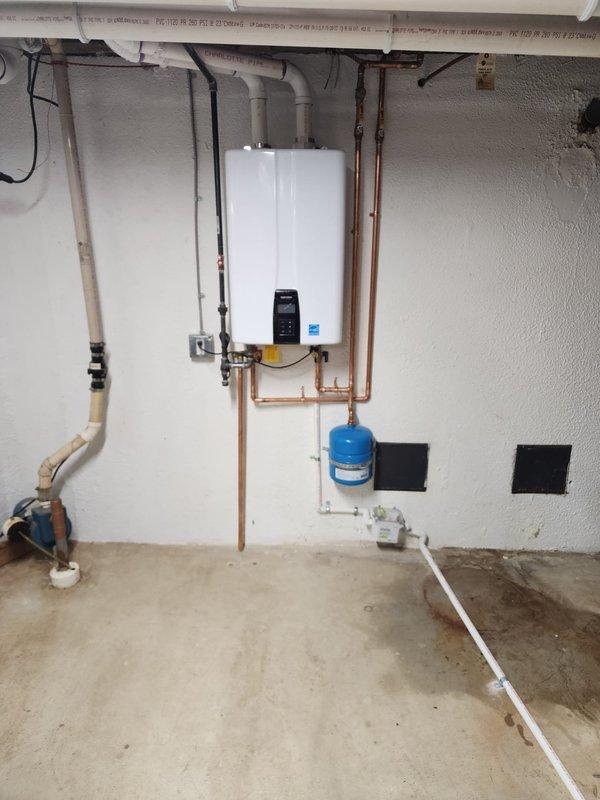 Completed installation of wall-mounted tankless water heater system in residential basement utility area. Installation included mounting primary unit to wall with proper support hardware, connecting copper supply and return lines, installing blue expansion tank, running white PVC exhaust and intake venting through ceiling structure, integrating electrical conduit and wiring to control panel, and ensuring all connections meet code requirements for safe operation.