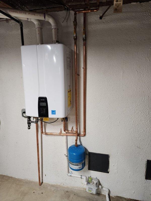 Completed installation of wall-mounted tankless water heater system in residential basement utility area. Installation included mounting primary unit to wall with proper support hardware, connecting copper supply and return lines, installing blue expansion tank, running white PVC exhaust and intake venting through ceiling structure, integrating electrical conduit and wiring to control panel, and ensuring all connections meet code requirements for safe operation.