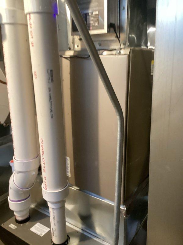 Completed HVAC system replacement including installation of new air handler unit with associated refrigerant lines, condensate drainage system, and ductwork connections. The installation features properly routed copper refrigerant lines, white PVC condensate piping with appropriate fittings and valves, filter drier component, and integrated metallic ductwork for air distribution. All components were installed in the mechanical room with proper clearances and connections verified for system operation.