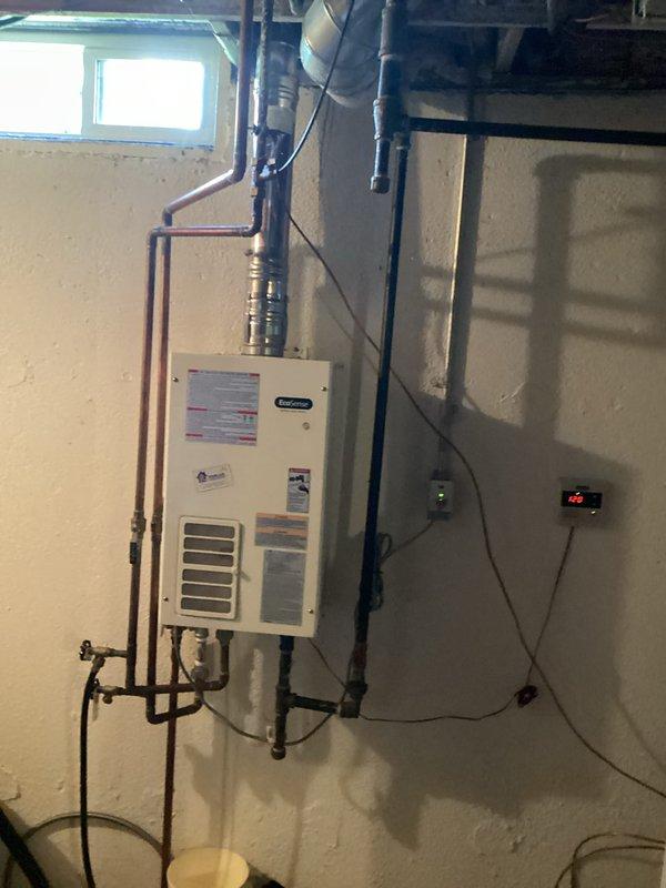 Completed water heater installation in basement utility area of 28-year-old residential property. Installed wall-mounted tankless water heater unit on concrete block wall with proper copper supply line connections and PVC venting integrated with existing HVAC ductwork. Established electrical connections to digital control panel, verified all piping connections for proper water flow, and ensured unit compliance with manufacturer specifications and safety requirements.