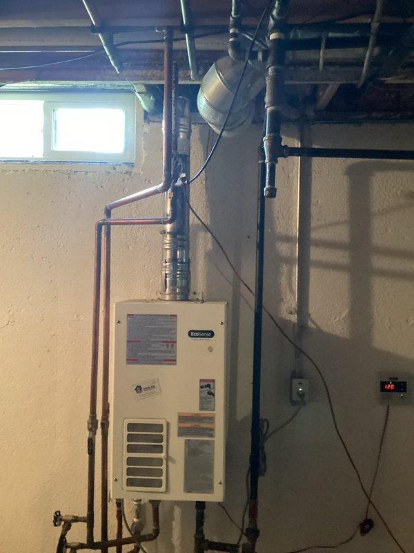 Completed water heater installation in basement utility area of 28-year-old residential property. Installed wall-mounted tankless water heater unit on concrete block wall with proper copper supply line connections and PVC venting integrated with existing HVAC ductwork. Established electrical connections to digital control panel, verified all piping connections for proper water flow, and ensured unit compliance with manufacturer specifications and safety requirements.