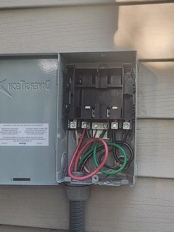 Responded to warranty call for missing dead front cover on outdoor A/C disconnect box. Upon arrival, found DiversiTech electrical disconnect enclosure mounted on exterior wall with cover panel removed, exposing internal fuse holders, terminal connections, and wiring. Inspected installation and verified all electrical connections were secure with proper wire routing through conduit. Confirmed disconnect box functionality and proper operation of safety components. Documentation photos captured current condition of unit showing open enclosure with visible terminal blocks, fuse holders, and color-coded wiring properly installed through flexible conduit. Unit remains operational pending replacement cover installation.