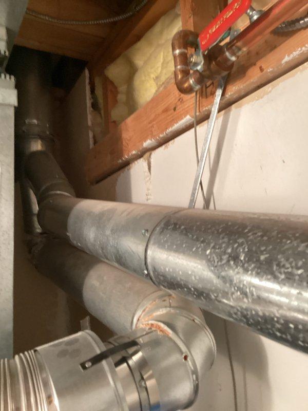 Completed on-site assessment of aging water heater system exhibiting active leakage. Documented existing installation including corroded cylindrical expansion tank or pressure vessel mounted atop water heater, copper supply lines with shutoff valves, and galvanized venting components showing mineral deposits and moisture damage. Photographed current plumbing configuration and identified failed components requiring replacement to provide accurate estimate for new water heater installation.