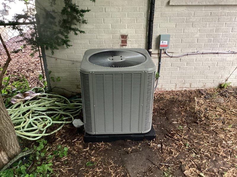 Completed installation of Lennox air conditioning system with outdoor condenser unit positioned on concrete pad against exterior brick wall. Unit was properly mounted, leveled, and connected to attic air handler with electrical disconnect and line set installed per manufacturer specifications.