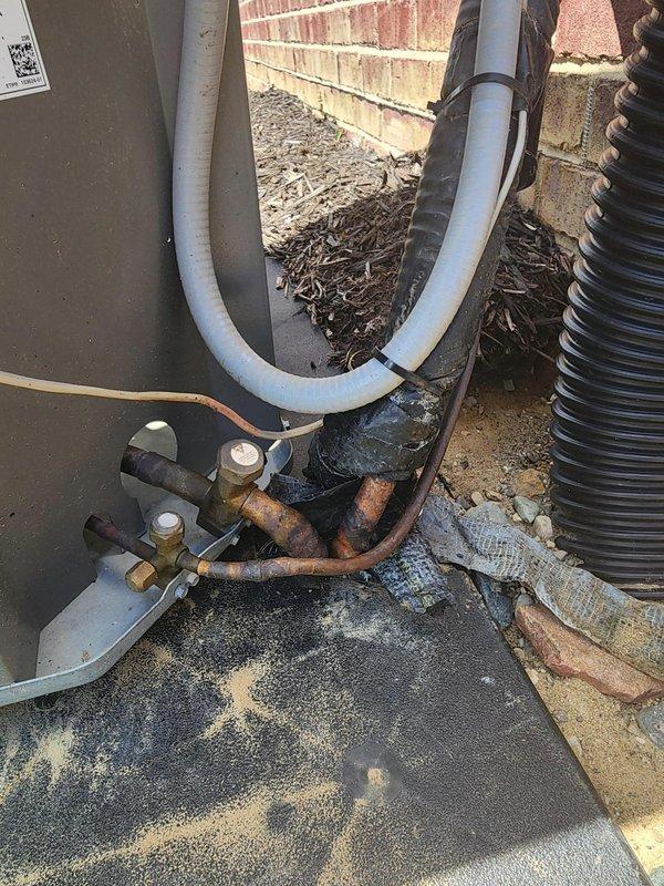 Responded to service call for outdoor A/C unit that had tipped over from window installation, causing damage to refrigerant line set. Upon arrival, found unit displaced from original position with severely bent and corroded copper refrigerant lines. Documented extensive rust and oxidation on line set and mounting hardware. Unit assessed for structural damage and line set integrity compromised due to physical displacement and prolonged exposure to elements.