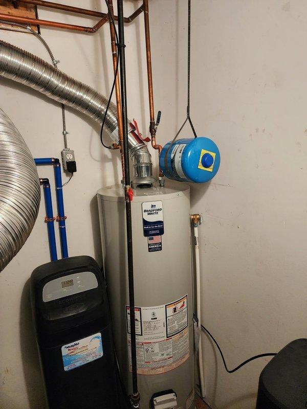Completed installation of 40-gallon Bradford White tanked water heater in residential utility room. Connected copper supply lines with shut-off valves, installed expansion tank, integrated unit with existing HVAC ductwork, and verified all plumbing connections, drain valve, and electrical components for proper operation.