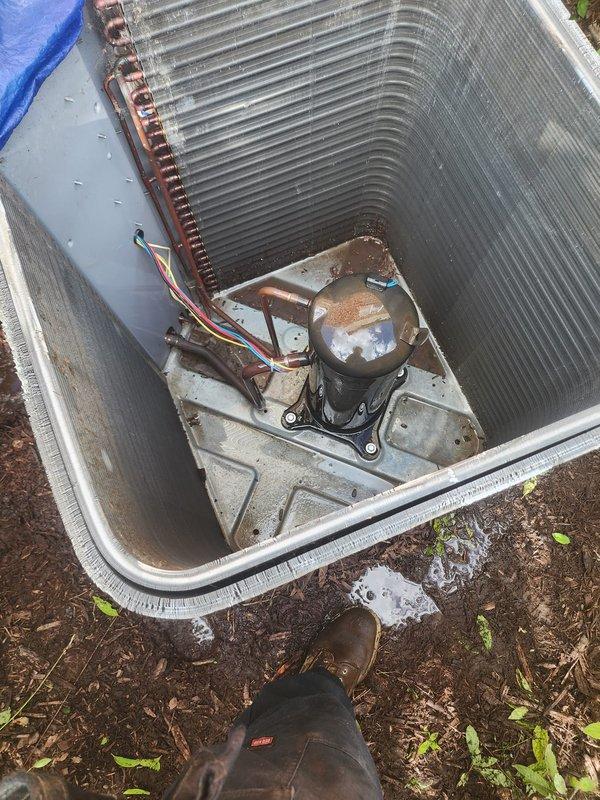 # HVAC Service Report - No Cooling Condition

Responded to service call for air conditioning unit not cooling. Upon arrival, found outdoor condenser unit located against brick exterior wall with landscaping surrounding the equipment. 

Removed top access panel to inspect internal components. Found 10+ year old unit with black cylindrical compressor, copper refrigerant lines, and U-shaped aluminum fin evaporator coil running perimeter of cabinet. Noted significant dust accumulation on coil surfaces and dirt buildup on interior base and compressor mounting area. Unit showed visible signs of age with weathering on components and some surface oxidation present.

Performed diagnostic inspection of compressor, electrical connections (red, yellow, and white wiring), and refrigerant lines. Assessed overall condition of evaporator coil with tightly-spaced aluminum fins. Documented equipment condition and findings with photographs for service records.

Given the age of the unit (10+ years) and o