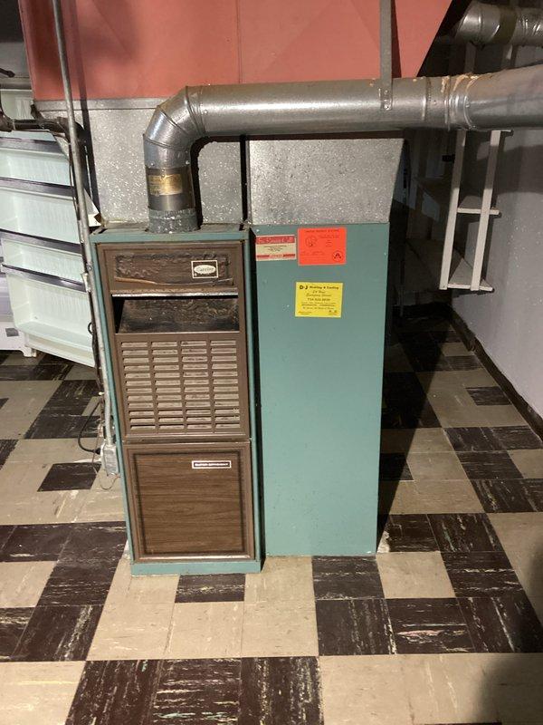 Conducted comprehensive HVAC system evaluation for residential property with existing 20+ year old equipment. Assessed furnace and air handler unit located in basement utility area, noting aged ductwork and original installation configuration. Evaluated exterior condensing unit and associated electrical components, documenting significant weathering and rust deterioration on disconnect box and conduit connections. Provided complete system replacement estimate for new homeowners, photographed existing equipment conditions including interior furnace assembly with brown wood-grain air handler cabinet and teal metal section, exterior brick-mounted electrical service components, and outdoor condensing unit placement. Current system operational but recommended replacement due to age and efficiency considerations.