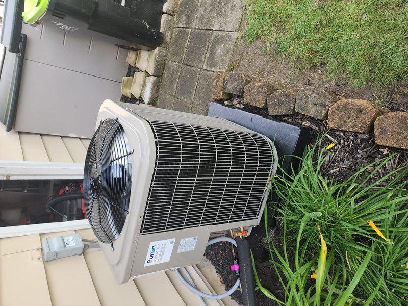 Completed installation of Bryant brand air conditioning condenser unit at residential property. Unit was positioned on concrete pad adjacent to building exterior beneath covered porch area, with all electrical connections, refrigerant lines, and condensate drainage properly installed and tested for optimal system performance.