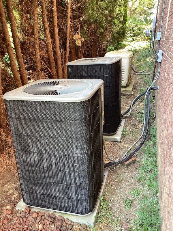 Completed on-site evaluation for air conditioning system replacement. Assessed existing dual outdoor condenser units located in side yard between brick structure and evergreen hedge, documented current equipment condition showing weathering and dirt accumulation on mesh grilles, photographed electrical conduit routing along brick wall and refrigerant line configurations, and evaluated installation space constraints in narrow access area with concrete pad foundation. Prepared comprehensive replacement estimate based on site conditions and equipment specifications.