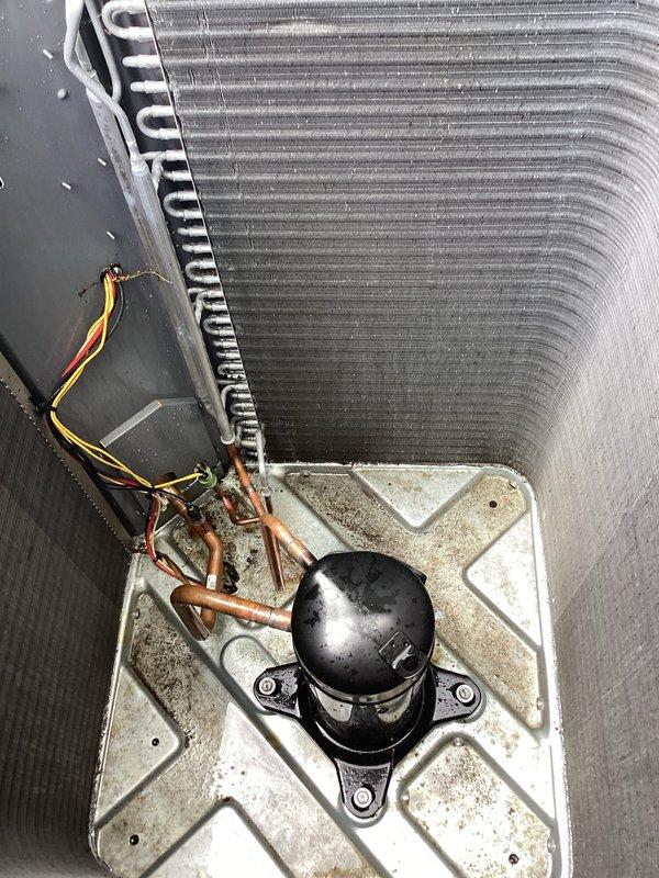 Responded to no-cooling complaint on 1-year-old residential air conditioning system located at rear of property. Upon arrival, confirmed unit was running but delivering warm air to occupied space with rising indoor temperatures. Performed comprehensive diagnostic evaluation of outdoor condensing unit and associated components. Visual inspection revealed compressor operation and electrical connections intact, with refrigerant lines and coil assembly showing normal oxidation consistent with equipment age. Conducted system performance testing and identified root cause of cooling failure. Due to urgency of situation and health considerations, documented findings with photographic evidence showing internal compressor assembly, refrigerant line connections, and external condenser unit condition. System components including evaporator/condenser coil, electrical wiring, and mounting hardware were assessed for proper installation and operational status.
