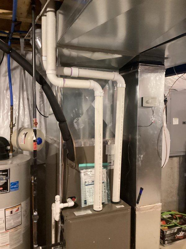Completed comprehensive assessment of existing HVAC system in residential basement mechanical room for air conditioning replacement estimate. Evaluated current furnace unit, associated ductwork, electrical connections, and condensate drainage system configuration. Documented existing equipment layout including proximity to water heater, electrical panel, and utility connections. Assessed available space for new air conditioning system installation, noting ceiling clearances and PVC piping routes. Photographed current mechanical room setup showing furnace positioning, white PVC condensate lines forming loop configuration at ceiling level, and existing electrical service panel. Evaluated structural considerations for equipment replacement including floor space, wall clearances, and access points for refrigerant line routing. Reviewed existing ductwork connections and determined compatibility requirements for new AC system integration with current heating equipment. Provided detailed phot