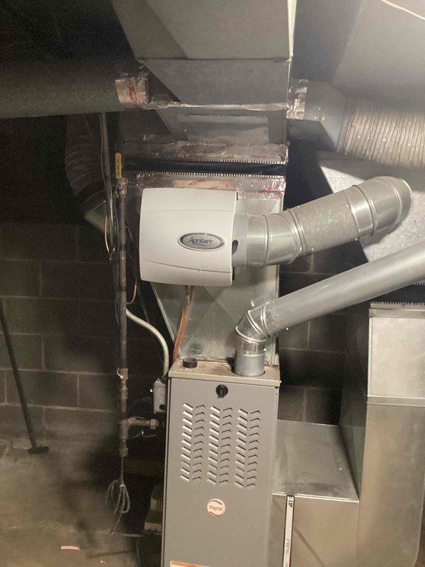 Completed comprehensive assessment of existing residential HVAC system located in basement mechanical room for equipment replacement estimate. Documented current installation consisting of beige/tan furnace unit with Aprilaire humidifier mounted on top, evaporator coil assembly, flexible and rigid ductwork configuration, and associated copper refrigerant lines. Photographed existing equipment layout, ductwork connections including silver flexible ducts and metallic rectangular supply/return runs, and overall mechanical room infrastructure to provide accurate replacement specifications and system sizing recommendations for customer consideration.
