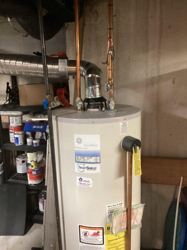 Performed water heater replacement estimate for leaking GE SmartWater residential tank-style unit showing moisture staining at base. Assessed existing installation including copper supply lines, yellow-handled shutoff valve, flexible connections, and venting system to provide replacement specifications before failure causes significant water damage.