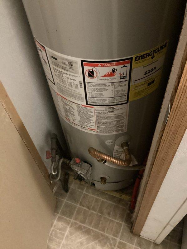 Performed replacement estimate for 20-year-old residential water heater experiencing degraded performance with rusty and odorous water output. Inspected existing unit installed in utility closet, documented current installation including plumbing connections, safety labels, and gas line configuration. Verified serial number SC411405569 indicating possible March 2018 manufacture date, assessed condition of surrounding components including shut-off valves and flexible connectors to provide accurate replacement specifications.