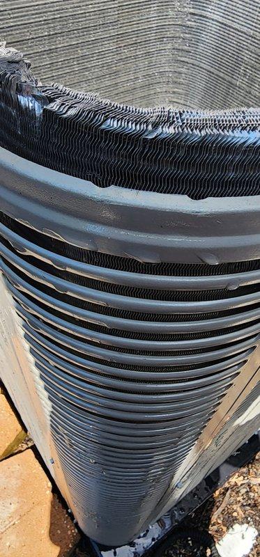 Completed routine maintenance on outdoor air conditioning unit and heat pump system. Inspected cylindrical condenser unit and documented significant accumulation of organic debris, dirt, and leaves along the top edge and between the horizontal metal fins. Debris buildup was particularly heavy in the upper rim area, indicating need for thorough cleaning to maintain optimal heat exchange efficiency. Examined interior air handler compartment and found extensive dirt and particulate matter coating interior surfaces with visible striations throughout. Verified compressor unit securely mounted with proper bracket installation and confirmed refrigerant lines properly connected. Unit operational but requires cleaning to restore full efficiency and prevent potential airflow restrictions that could impact system performance.