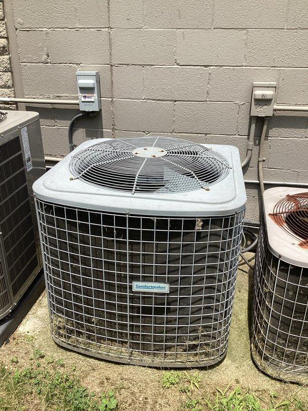 Completed commercial HVAC estimate for replacement of AC unit 2-4, documenting existing outdoor condenser equipment mounted on exterior concrete block wall with associated electrical disconnects and conduit routing. Photographed current installation showing multiple condensing units with weathered protective grilles, electrical service panels, and ground-level positioning to support replacement specifications and equipment requirements.