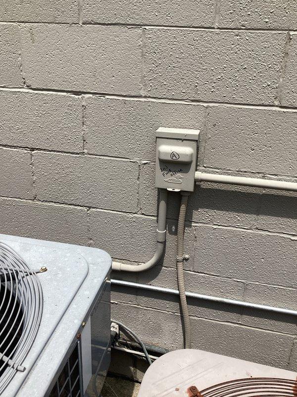 Completed commercial HVAC estimate for replacement of AC unit 2-4, documenting existing outdoor condenser equipment mounted on exterior concrete block wall with associated electrical disconnects and conduit routing. Photographed current installation showing multiple condensing units with weathered protective grilles, electrical service panels, and ground-level positioning to support replacement specifications and equipment requirements.