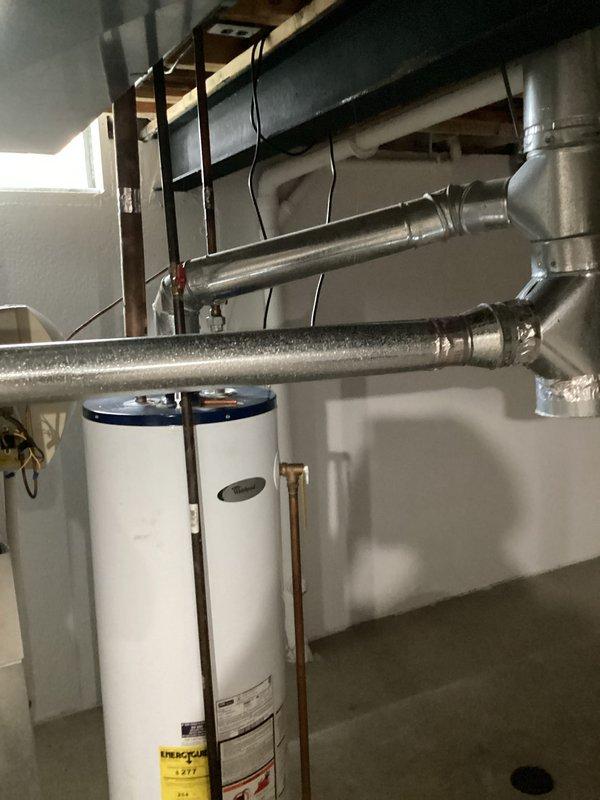 Conducted on-site evaluation of existing residential water heater installation in basement utility room. Assessed current white cylindrical water heater unit with standard venting configuration, including metal ductwork connections and copper supply piping. Documented equipment specifications, clearances, and existing plumbing connections to prepare comprehensive replacement estimate for 10-12 year old unit approaching end of service life.