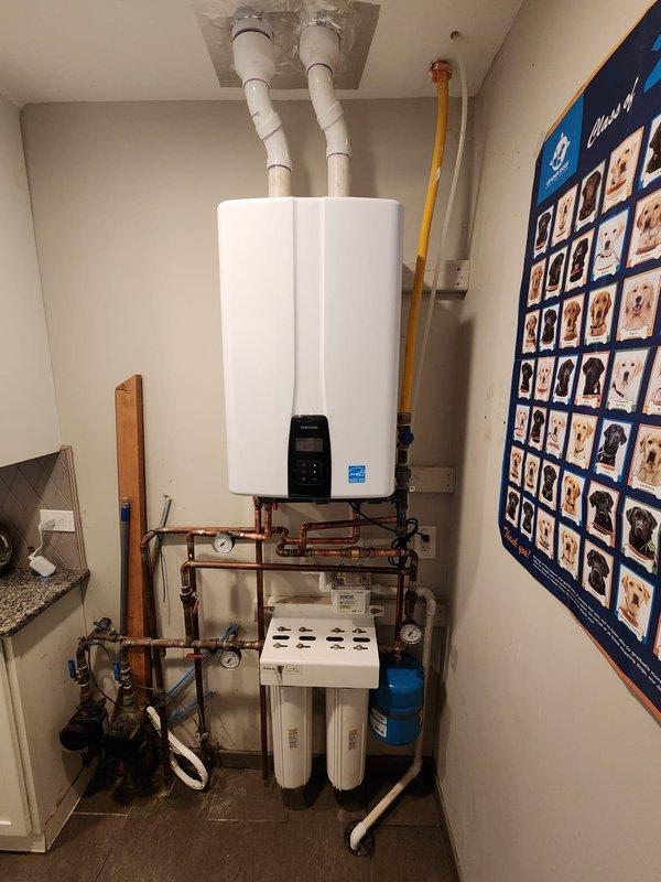 Successfully replaced existing water heater with new wall-mounted tankless unit in utility room. Installation included complete venting system with PVC exhaust pipes, comprehensive copper supply and return line configuration with integrated shut-off valves and pressure gauges for system monitoring and maintenance access. Installed dual-stage whole-house water filtration system at base of unit with easily accessible filter housings, along with blue expansion tank for thermal expansion protection. All connections tested and verified for proper operation, with digital control panel programmed and Energy Star certified unit confirmed operational.