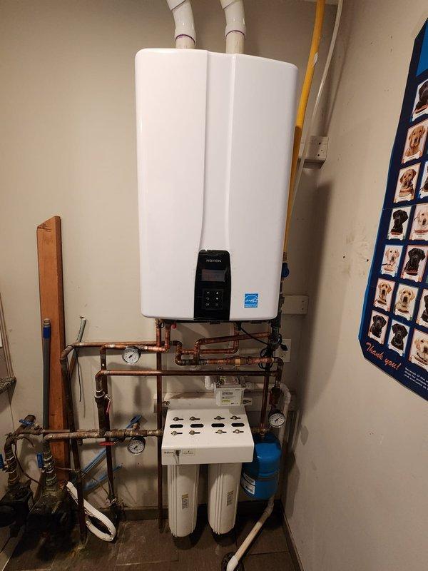 Successfully replaced existing water heater with new wall-mounted tankless unit in utility room. Installation included complete venting system with PVC exhaust pipes, comprehensive copper supply and return line configuration with integrated shut-off valves and pressure gauges for system monitoring and maintenance access. Installed dual-stage whole-house water filtration system at base of unit with easily accessible filter housings, along with blue expansion tank for thermal expansion protection. All connections tested and verified for proper operation, with digital control panel programmed and Energy Star certified unit confirmed operational.