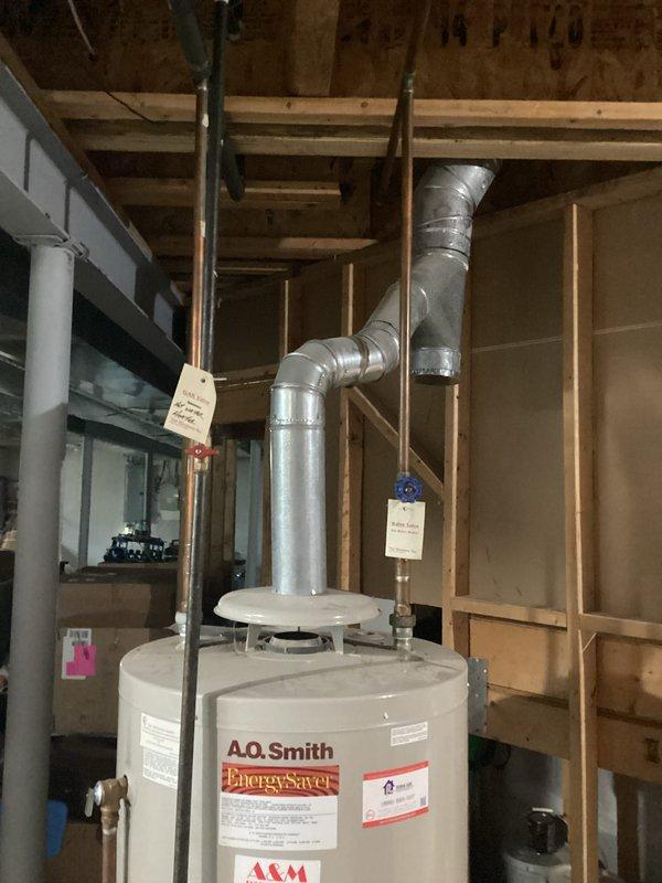 Completed water heater installation estimate for an A.O. Smith Energy Saver unit located in an unfinished basement area with exposed framing. Assessed existing plumbing connections, venting requirements through flexible metal ductwork configured in an L-shape routing, and documented current installation specifications including copper and black pipe connections at the unit's top terminus.