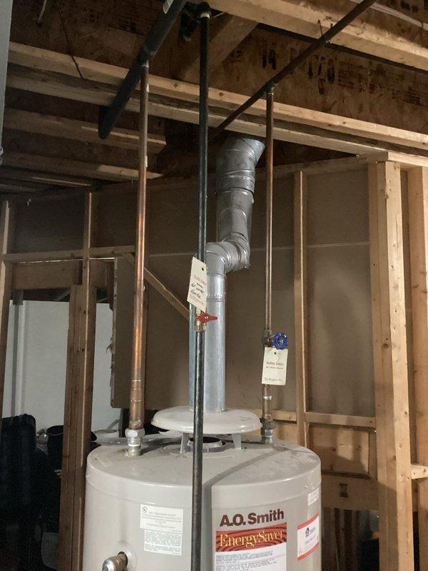 Completed water heater installation estimate for an A.O. Smith Energy Saver unit located in an unfinished basement area with exposed framing. Assessed existing plumbing connections, venting requirements through flexible metal ductwork configured in an L-shape routing, and documented current installation specifications including copper and black pipe connections at the unit's top terminus.