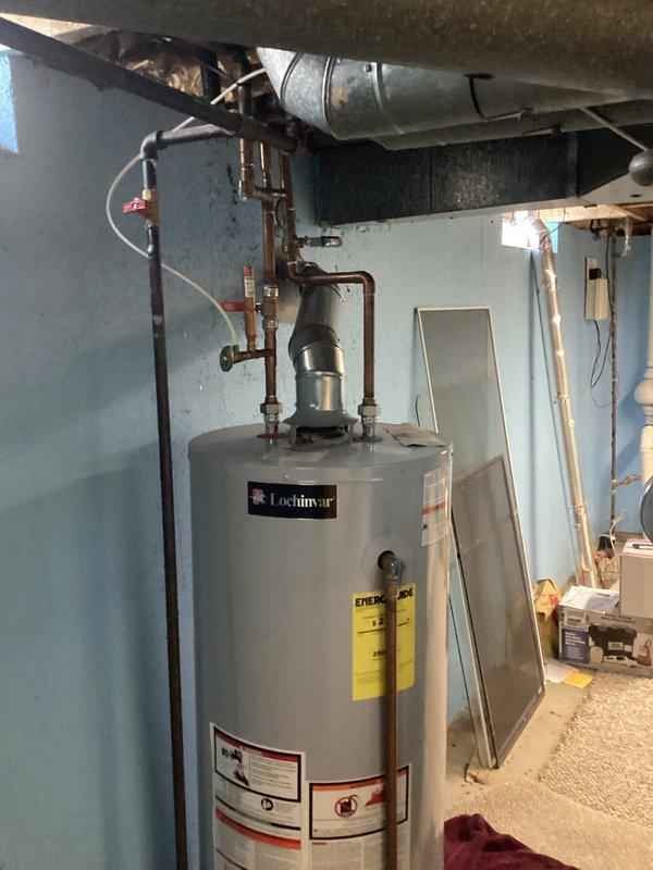 Conducted assessment of existing Lochinvar water heater located in basement mechanical room for replacement estimate. Evaluated installation configuration including copper supply piping, pressure relief valve system, and venting arrangement with metal exhaust duct. Noted limited drainage options available for tank removal, with only laundry sink accessible for water disposal during replacement process. Documented current unit specifications, connection points, and clearances in utility space with exposed floor joists and concrete flooring. Photographed existing installation to provide comprehensive documentation for replacement planning and material requirements.