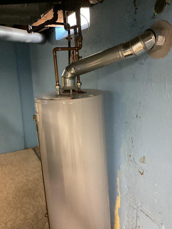 Conducted assessment of existing Lochinvar water heater located in basement mechanical room for replacement estimate. Evaluated installation configuration including copper supply piping, pressure relief valve system, and venting arrangement with metal exhaust duct. Noted limited drainage options available for tank removal, with only laundry sink accessible for water disposal during replacement process. Documented current unit specifications, connection points, and clearances in utility space with exposed floor joists and concrete flooring. Photographed existing installation to provide comprehensive documentation for replacement planning and material requirements.