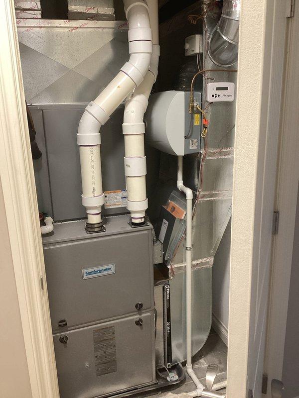 Responded to service call for non-operational air conditioning system and outdoor condenser unit. Evaluated existing nine-year-old four-ton HVAC system with condenser located outside near garage and air handler positioned upstairs. Conducted comprehensive assessment of both indoor and outdoor equipment to determine failure points and system viability. Documented current installation including ComfortMaker air handler unit, associated ductwork, PVC condensate drainage lines, and ventilation components. Photographed existing equipment configuration showing metallic air handler with proper condensate piping, white PVC exhaust/intake venting, and standard residential HVAC installation setup. Provided detailed replacement estimate for complete four-ton system upgrade to address equipment failure and restore cooling functionality to residence.