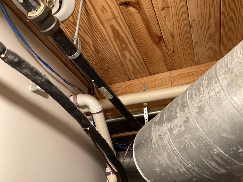 Completed warranty inspection on HVAC equipment installation to verify compliance with manufacturer specifications. Documented existing vent piping configuration with photographs showing PVC exhaust system and metal ductwork in ceiling space, along with water heater and associated plumbing connections. Installation manual acquisition required to determine if cellular core vent piping replacement with solid core piping is necessary per manufacturer requirements.