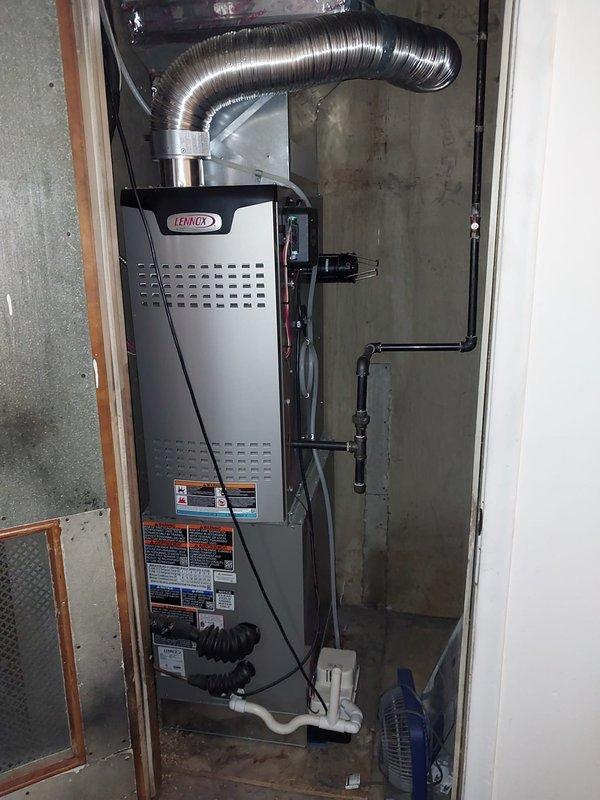 Responded to service call for cracked and leaking condensate drain line. Upon inspection, identified damaged 8-12 inch section of drain piping on exterior of building beneath roofline. Documented existing conditions showing deteriorated black flexible drain hose and associated white PVC drainage components mounted along siding near gutter system. Photographed Lennox furnace unit in mechanical room to verify condensate source and drainage configuration. Completed warranty repair of compromised drain line section to restore proper condensate drainage and eliminate water leakage.