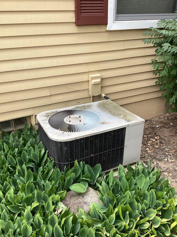 Performed comprehensive assessment of residential air conditioning system found to be low on R-22 refrigerant. The outdoor condensing unit showed significant age-related deterioration with visible weathering, dirt accumulation, and staining on the cabinet surfaces. Given the system's use of R-22 refrigerant, which is being phased out and has become increasingly expensive, combined with the unit's apparent age and condition, recommended full system replacement rather than repair. Documented existing outdoor unit installation against home exterior and indoor furnace/air handler configuration in basement mechanical room for replacement planning purposes.
