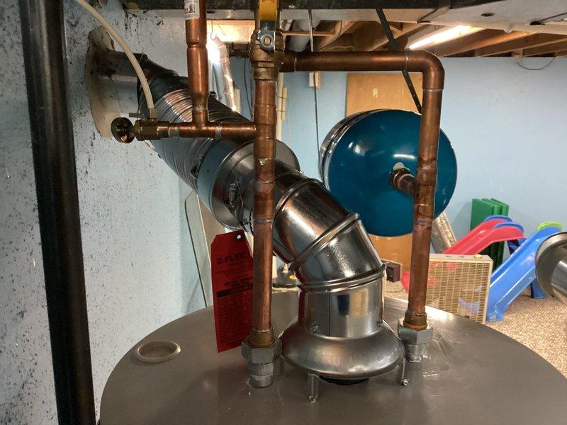 Completed installation of a 50-gallon Bradford White tanked water heater in basement utility room. Connected copper supply and discharge piping to unit with proper shutoff valves and fittings, installed blue expansion tank on wall to manage thermal expansion in closed plumbing system, and ran black TPR discharge pipe vertically along side of unit per code requirements. All connections pressure tested and water heater commissioned successfully with proper venting configuration confirmed.