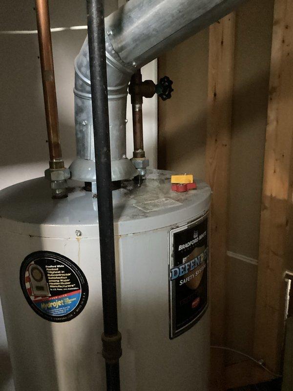 Completed water heater estimate for Bradford White Defender Safety System unit located in unfinished basement utility area. Inspected existing installation including copper and galvanized piping connections, brass valve assembly, and exhaust vent ductwork. Documented current water heater configuration with cold water inlet, hot water outlet, and HVAC duct routing through overhead joists. Account information verified and photographic documentation captured for estimate preparation.