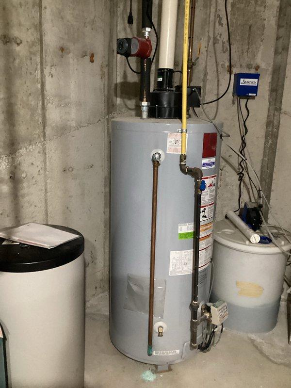 Conducted comprehensive assessment of existing water heater installation in basement mechanical room for replacement estimate. Evaluated current unit configuration including gas supply line, circulation pump with electrical components, copper piping connections, and venting system. Documented existing setup showing water heater positioned between water softener and secondary storage tank, with digital controller mounted on wall for system management. Inspected overhead venting and ductwork routing through ceiling structure. Assessed accessibility for replacement work and photographed all mechanical connections, gas line placement, electrical wiring, and surrounding equipment to provide accurate replacement estimate. No active service issues reported with current unit.