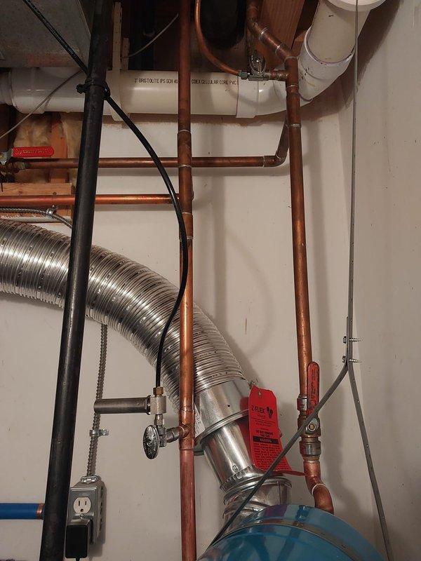 Completed warranty inspection and corrections on Bradford White water heater installation. Addressed three code compliance issues: repositioned temperature and pressure relief valve to provide adequate clearance from wall for proper operation and future replacement access, installed required safety drain pan beneath water heater per Section 504.7 through 504.7.2 of the 2021 Michigan Plumbing Code, and secured flexible vent connections to water heater and chimney with appropriate screws. Documentation photos captured of corrected installation showing properly positioned relief valve, compliant drain pan installation, and secured vent connections along with associated copper piping, blue expansion tank, and mechanical room components.