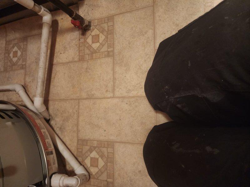 Completed installation of 40-gallon tanked water heater in utility room with ceramic tile flooring. Connected supply lines with shut-off valves and installed white PVC discharge piping in accordance with plumbing code requirements. Unit is operational and ready for service.