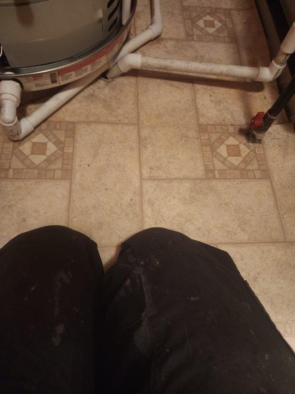 Completed installation of 40-gallon tanked water heater in utility room with ceramic tile flooring. Connected supply lines with shut-off valves and installed white PVC discharge piping in accordance with plumbing code requirements. Unit is operational and ready for service.